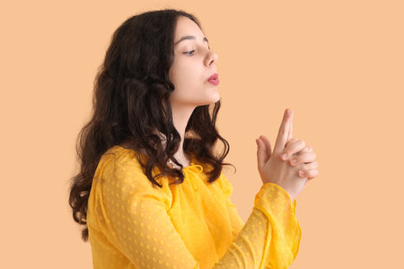 Teenage girl in yellow dress showing gun gesture on beige backgroundの写真素材