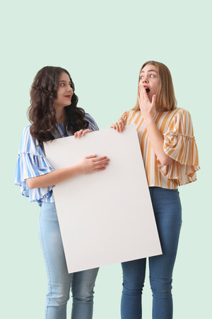 Young women with big blank poster on mint backgroundの写真素材