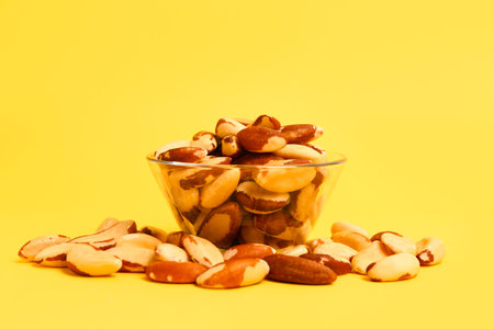 Bowl of tasty Brazil nuts on yellow background