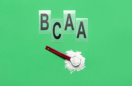 Scoop of amino acid supplement and letters BCAA on green background