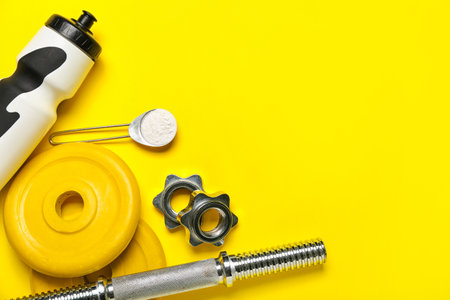 Barbell plates, grip, bottle of water and scoop with amino acid supplement on yellow backgroundの写真素材