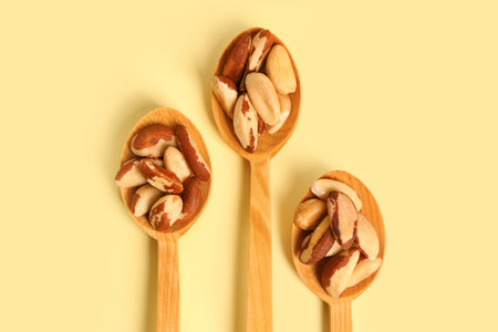 Wooden spoons of tasty Brazil nuts on yellow background, closeup