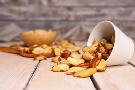 Overturned bowl of tasty Brazil nuts on light wooden tableの写真素材