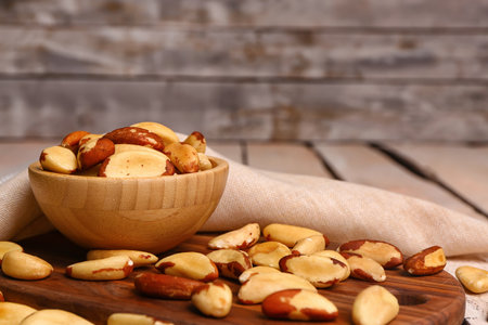 Board with bowl of tasty Brazil nuts on light wooden table, closeupの写真素材
