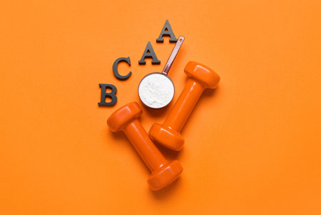 Letters BCAA, scoop with amino acid supplement and dumbbells on color backgroundの写真素材