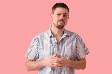 Upset young man in shirt on pink backgroundの写真素材