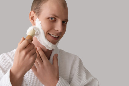 Young man applying shaving foam on face against light backgroundの写真素材