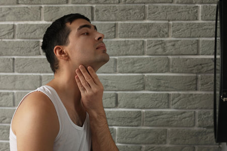 Young man with bristle on his face looking in mirror at homeの写真素材