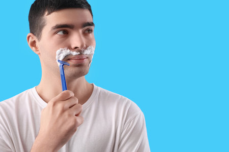 Young man shaving against light blue backgroundの写真素材