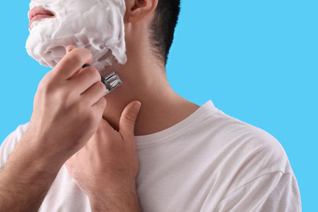 Young man shaving against light blue background, closeupの写真素材
