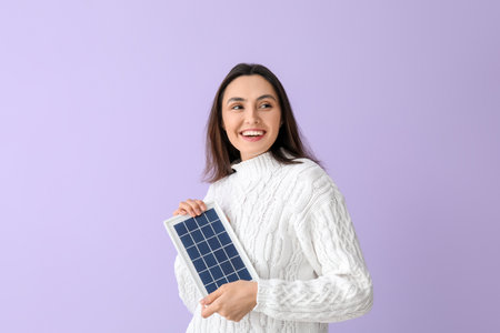 Pretty young woman with portable solar panel on lilac backgroundの写真素材