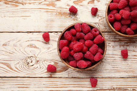 Bowls with fresh raspberries on wooden background