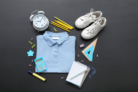 Stylish school uniform with alarm clock and different stationery on black chalkboardの写真素材