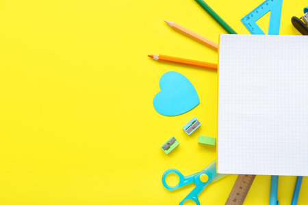 Frame made of different stationery with blank notebook on yellow background