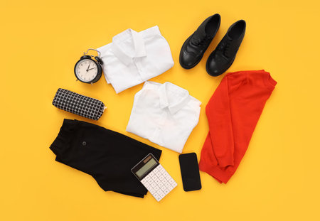 Composition with stylish school uniform, alarm clock, mobile phone and stationery on orange backgroundの写真素材