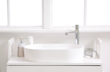 White sink with bath accessories on table in light bathroomの写真素材