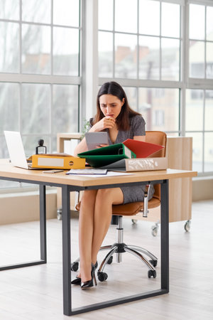 Stressed female accountant working with documents and calculator at table in officeの写真素材