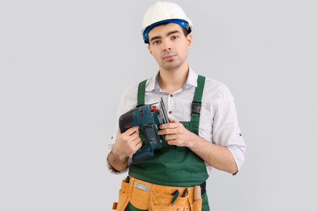 Young carpenter with cordless jigsaw on gray background