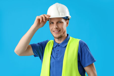 Male worker in vest and hardhat on blue background