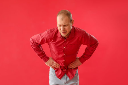 Young man with appendicitis on red backgroundの写真素材