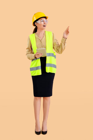 Female engineer in vest and with tablet computer pointing at something on beige backgroundの写真素材