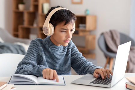 Little boy in headphones with book using laptop at homeの写真素材