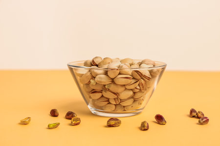Glass bowl with pistachio nuts and kernels on orange tableの写真素材