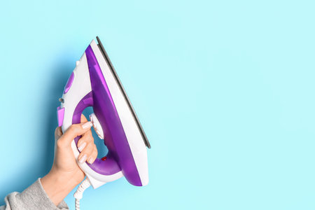Woman holding electric iron on blue backgroundの写真素材