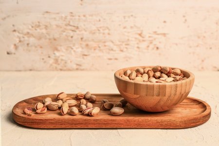 Board and bowl with tasty pistachio nuts on beige table
