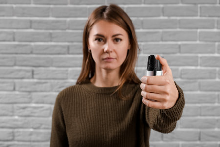 Young woman with pepper spray for self-defence on gray brick background, closeupの写真素材