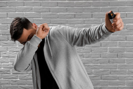 Young man with pepper spray for self-defence on gray brick background