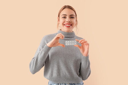 Beautiful young woman with blister of vitamin supplements on beige backgroundの写真素材