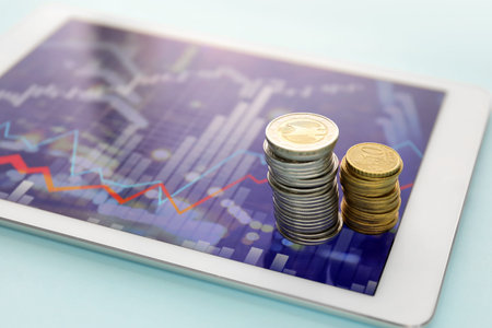 Coins and tablet computer with diagram of exchange rate on blue background