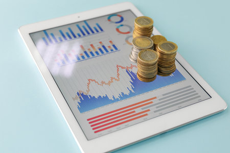 Tablet computer with diagrams of exchange rates and coins on blue backgroundの写真素材