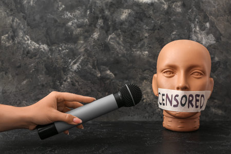 Woman holding microphone and taped human head with word CENSORED on dark table
