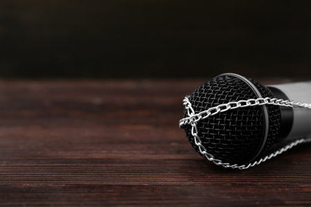 Microphone with chains on dark wooden background, closeup. Censorship conceptの写真素材
