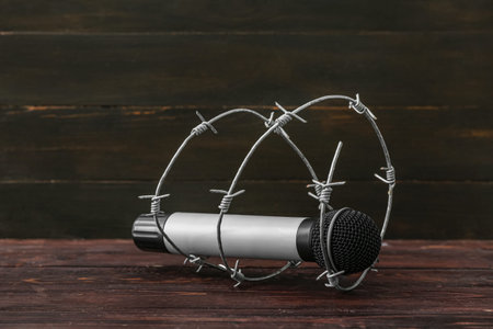 Microphone with barbed wire on dark wooden background. Censorship concept