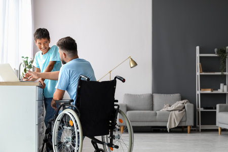 Little boy and his father in wheelchair using laptop at homeの写真素材