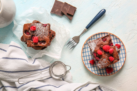 Baking paper and plate with pieces of raspberry chocolate brownie on light blue tableの写真素材