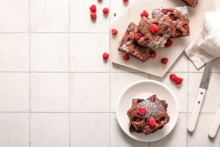 Board and plate with pieces of raspberry chocolate brownie on white tile backgroundの写真素材