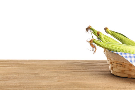 Wicker basket with fresh corn cobs on wooden table against white backgroundの写真素材