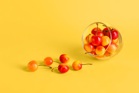 Glass with sweet yellow cherry on color backgroundの写真素材