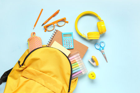 Backpack with calculator, headphones and different stationery on blue backgroundの写真素材