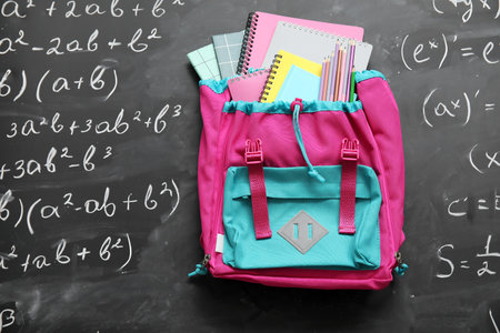Colorful school backpack with notebooks and pencils on black chalkboard painted with formulasの写真素材