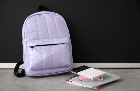 Lilac school backpack with notebooks and calculator on gray grunge table near black chalkboard