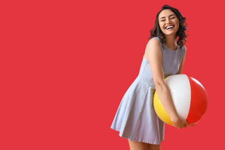 Young woman with beach ball on red backgroundの写真素材