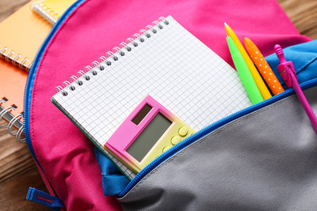 Backpack with blank notebook and stationery on brown wooden background