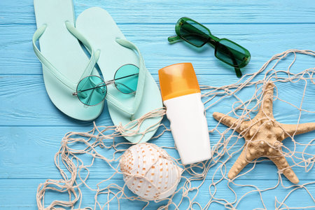 Net with flip flops, sunglasses and bottle of sunscreen cream on blue wooden background