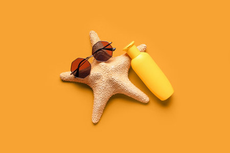 Creative composition with starfish, sunglasses and bottle of sunscreen cream on orange backgroundの写真素材