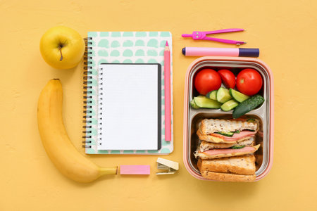 Different stationery and lunch box with tasty food on yellow backgroundの写真素材
